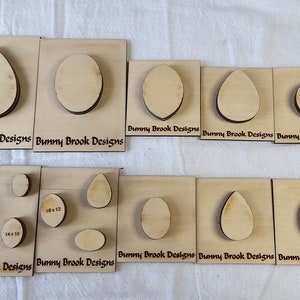 May include: A set of 10 wooden shapes for crafting, including circles, ovals, and teardrop shapes. The shapes are cut from natural wood and range in size from 1.5 inches to 2.5 inches. The shapes are labeled with their dimensions in inches. The text "Bunny Brook Designs" is printed on each piece.