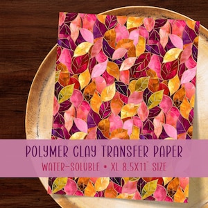 Op de afbeelding: Een vel wateroplosbaar polymeerklei transferpapier met een dicht, overlappend patroon van herfstkleurige bladeren in tinten goud, oranje, roze en dieppaars met dunne gouden omlijningen. De tekst luidt POLYMER CLAY TRANSFER PAPER WATER-SOLUBLE XL 8.5X11 SIZE.