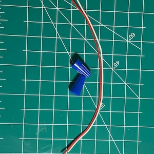May include: Two blue wire connectors and three wires, one white, one red, and one brown, on a green cutting mat.