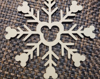 May include: A wooden snowflake ornament with Mickey Mouse ears on each point. The snowflake is cut out of a light brown wood and has a hole at the top for hanging.