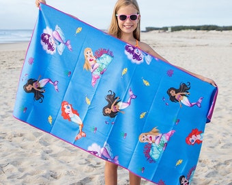 Può includere: Un telo mare blu con un motivo a sirene. L'asciugamano ha un bordo rosa ed è decorato con varie sirene con diversi colori di capelli e pesci. L'asciugamano è tenuto da una persona su una spiaggia sabbiosa.