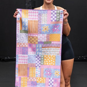 May include: A colourful patterned microfiber towel with a patchwork design featuring various geometric shapes, flowers, and abstract patterns in shades of pink, blue, yellow, and orange.