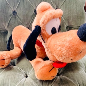May include: A plush brown and black dog toy with a red tongue. The dog is lying on a green sofa.