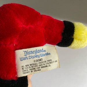 May include: A red, black and yellow plush toy with a Disneyland and Walt Disney World tag attached. The tag reads "Disneyland Walt Disney World" and "DISNEY ALL NEW MATERIALS POLYESTER FIBERS HE 1525 PA 401(KR) OHIO PA 1378-MASS T-616 CANASA TRADING CORP BURBANK, CA, PRODUCT OF SRILANKA".