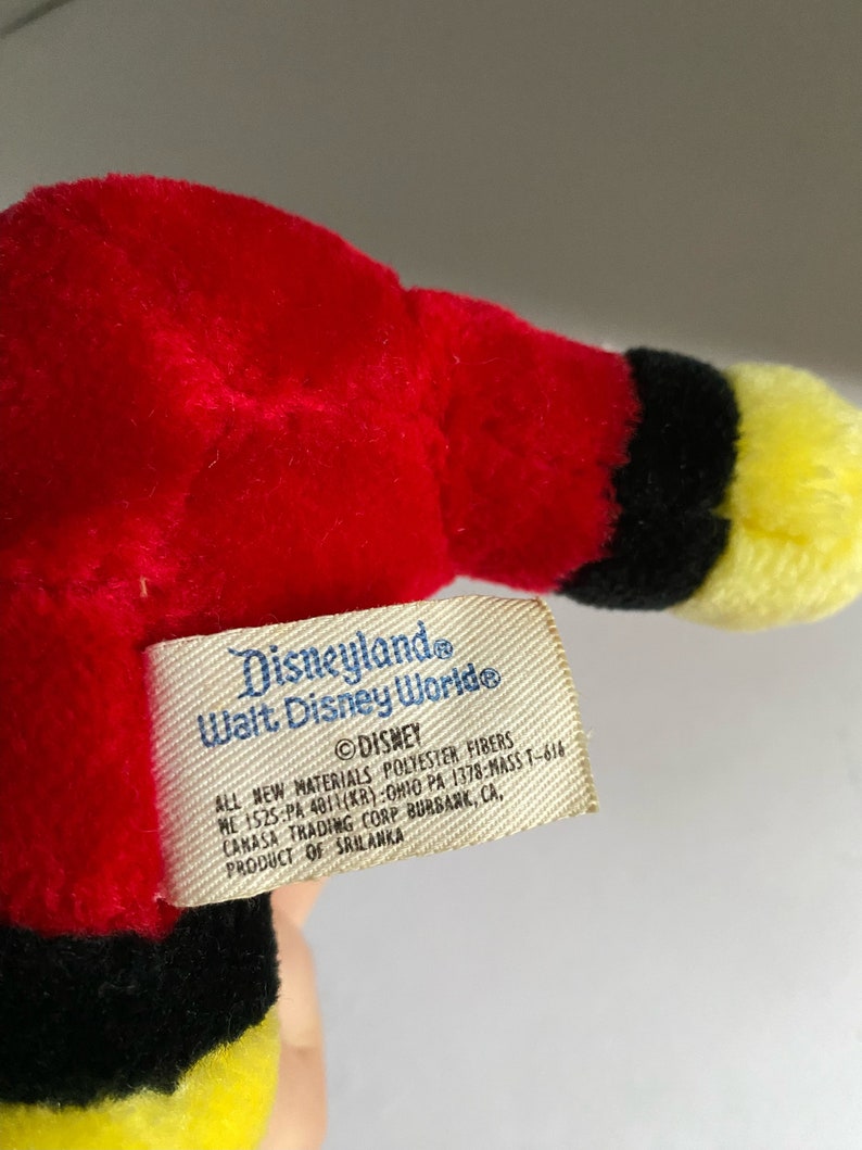 May include: A red, black and yellow plush toy with a Disneyland and Walt Disney World tag attached. The tag reads "Disneyland Walt Disney World" and "DISNEY ALL NEW MATERIALS POLYESTER FIBERS HE 1525 PA 401(KR) OHIO PA 1378-MASS T-616 CANASA TRADING CORP BURBANK, CA, PRODUCT OF SRILANKA".