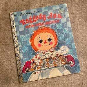 May include: A vintage Little Golden Book featuring Raggedy Ann and the Cookie Snatcher. The cover features a colorful illustration of Raggedy Ann holding a tray of cookies.