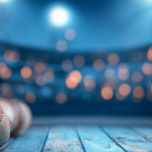May include: Several baseballs with red stitching are arranged on a weathered, light blue wooden surface. The background is a blurred view of a stadium, with soft, out-of-focus lights creating a bokeh effect.