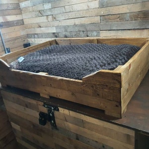 May include: A wooden dog bed with a brown blanket inside. The bed is made of reclaimed wood and has a rustic look.