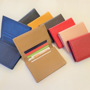 May include: A collection of leather wallets in various colors, including blue, tan, black, yellow, red, and pink. One wallet is open, displaying cards and cash. The wallets have a textured surface.