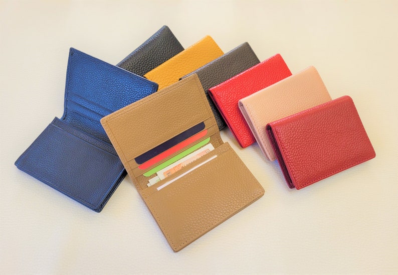 May include: A collection of leather wallets in various colors, including blue, tan, black, yellow, red, and pink. One wallet is open, displaying cards and cash. The wallets have a textured surface.