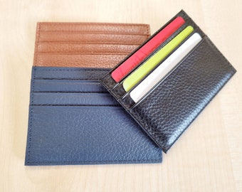May include: Two leather card holders, one blue and one black. The black card holder has three cards inside, one red, one green, and one white.