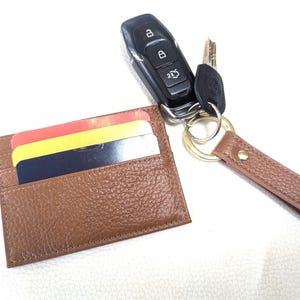 May include: A brown leather card holder with a key chain attached. The key chain has a gold key ring and a brown leather strap. The card holder has three cards inside.