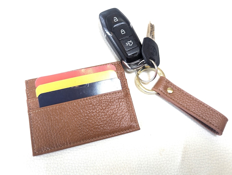 May include: A brown leather card holder with a key chain attached. The key chain has a gold key ring and a brown leather strap. The card holder has three cards inside.
