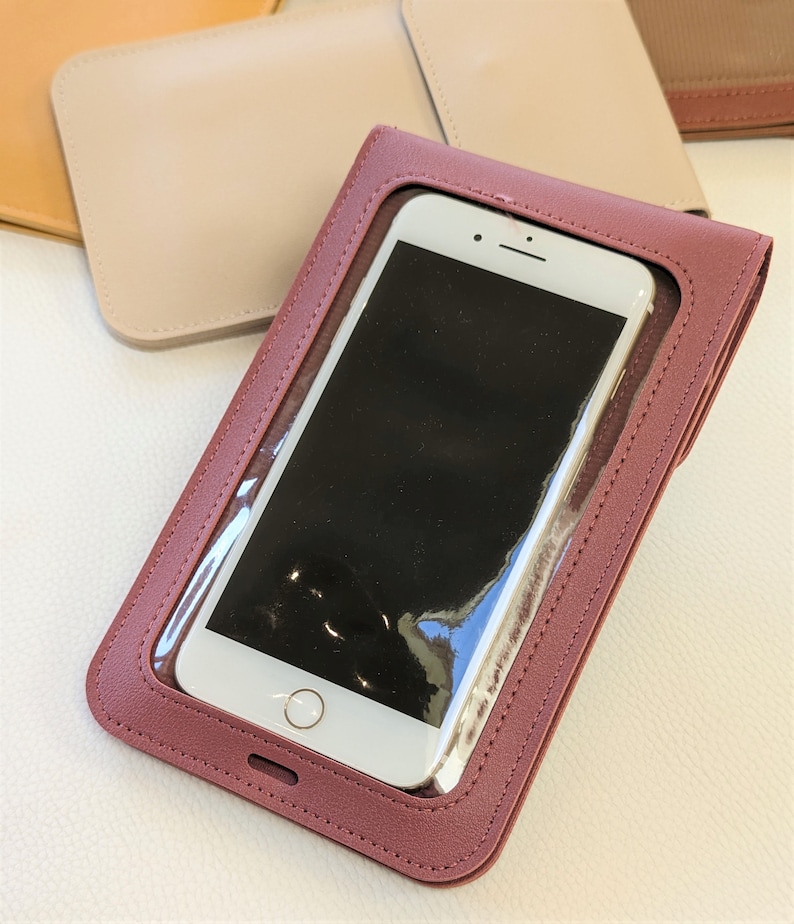 May include: A burgundy leather phone case with a clear plastic window to display a smartphone. The case has a stitched edge and a small hole at the bottom.