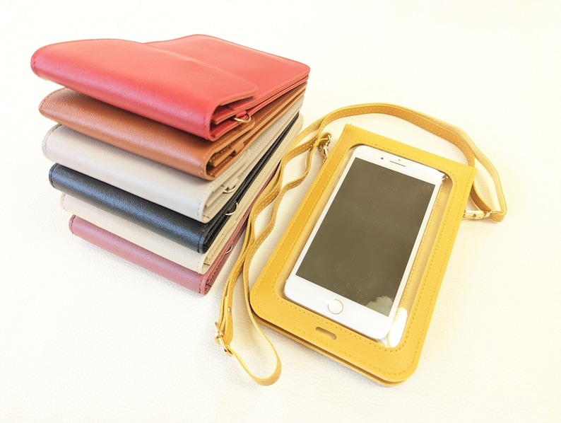 May include: A stack of six different colored leather wallets with a yellow phone case with a clear window for a phone. The phone case has a gold chain strap.