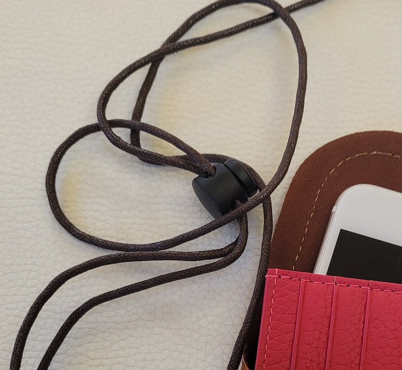May include: A pink leather phone case with a brown leather flap and a black adjustable strap. The case has a slot for a phone and a card holder.