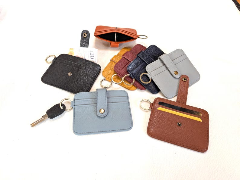 May include: A collection of leather cardholders in various colors, including black, brown, blue, gray, yellow, and burgundy. Each cardholder has a key ring and a snap closure. Some have a small strap.