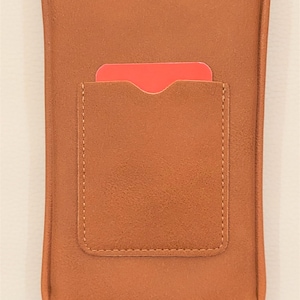 May include: A brown leather phone case with a flap pocket on the back. The case has a strap for carrying it over the shoulder.