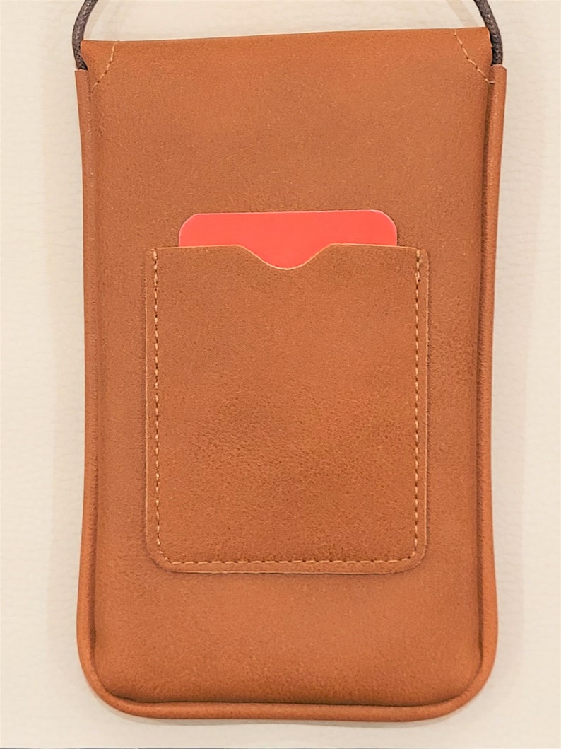 May include: A brown leather phone case with a flap pocket on the back. The case has a strap for carrying it over the shoulder.
