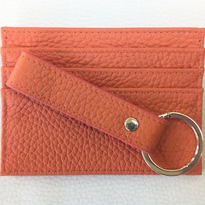 May include: A coral orange leather card holder with a key ring. The card holder has multiple slots for cards and a leather strap.