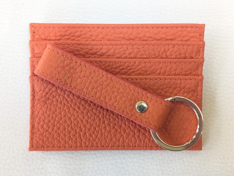 May include: A coral orange leather card holder with a key ring. The card holder has multiple slots for cards and a leather strap.
