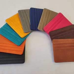 May include: A set of ten leather card holders in various colors, including teal, orange, black, brown, yellow, pink, gray, and blue. The card holders are arranged in a semi-circle.