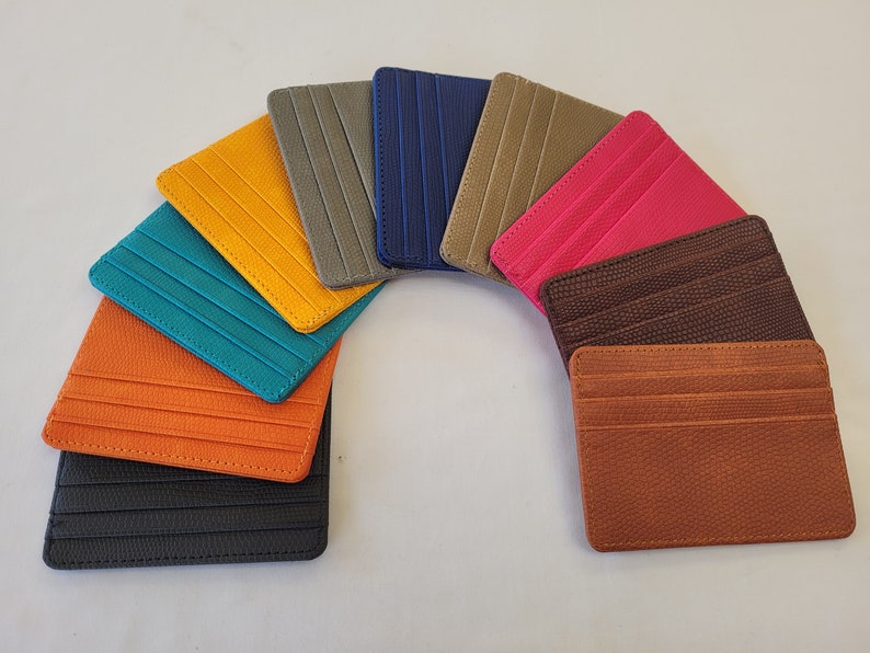 May include: A set of ten leather card holders in various colors, including teal, orange, black, brown, yellow, pink, gray, and blue. The card holders are arranged in a semi-circle.