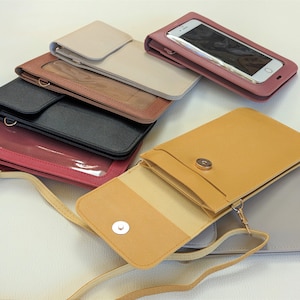 May include: Assortment of six phone crossbody bags in various colors, including beige, brown, black, red, yellow, and gray. Each bag has a clear plastic window for viewing a phone screen and a flap closure with a snap button.