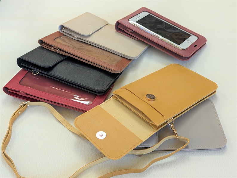 May include: Assortment of six phone crossbody bags in various colors, including beige, brown, black, red, yellow, and gray. Each bag has a clear plastic window for viewing a phone screen and a flap closure with a snap button.