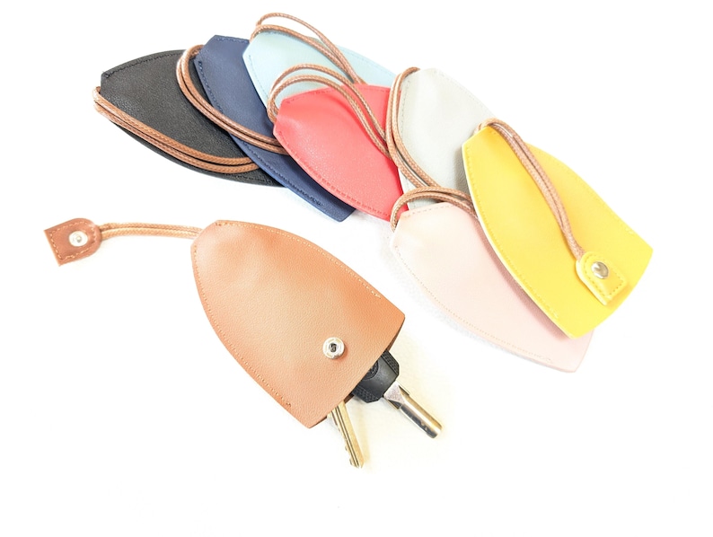 May include: A set of nine leather keychains in various colors, including black, blue, light blue, red, white, pink, and yellow. Each keychain has a loop for attaching keys and a small button closure.