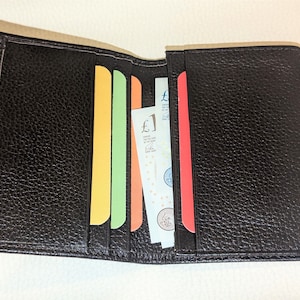 May include: Open black leather wallet with colorful card slots. The wallet contains paper currency and several brightly colored cards. The leather has a textured appearance.