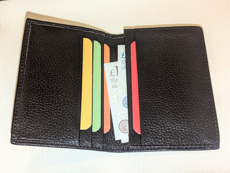 May include: Open black leather wallet with colorful card slots. The wallet contains paper currency and several brightly colored cards. The leather has a textured appearance.