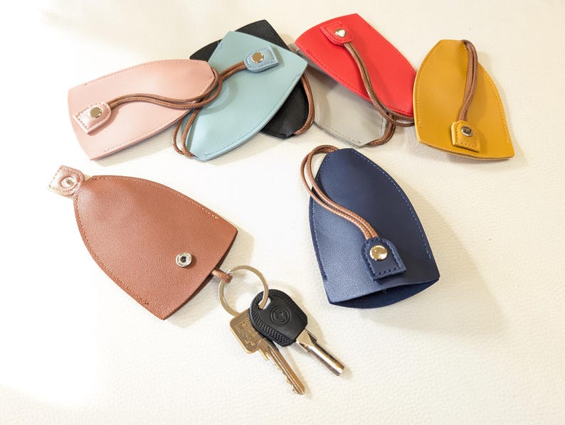 May include: Assortment of leather keychains in various colors, including brown, blue, yellow, red, and light blue. Each keychain has a metal snap closure and a loop for attaching keys. One keychain is shown with a set of keys.