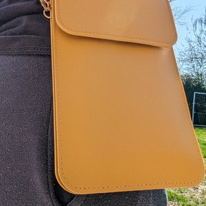 May include: A mustard yellow leather crossbody bag with a flap closure and a gold chain strap.