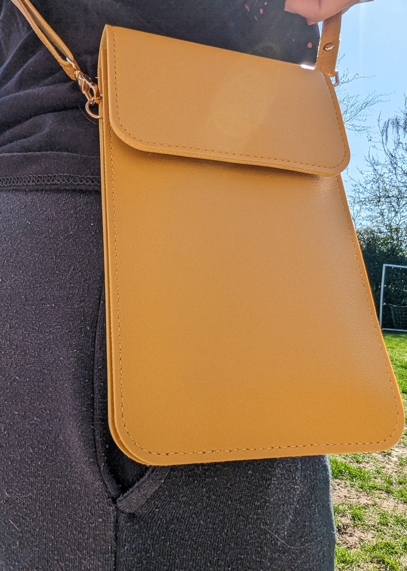 May include: A mustard yellow leather crossbody bag with a flap closure and a gold chain strap.