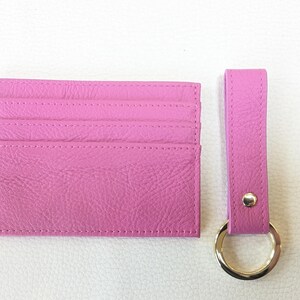 May include: A pink leather card holder with six card slots and a matching pink leather key chain with a gold ring.