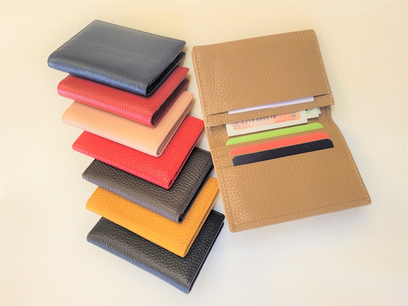 May include: A collection of leather wallets in various colors, including navy, red, tan, and yellow. One wallet is open, displaying cards and cash. The wallets have a textured finish and a classic design, suitable for carrying essentials.