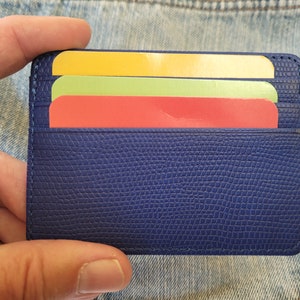 May include: A blue leather card holder with three cards inside. The cards are yellow, green, and red.