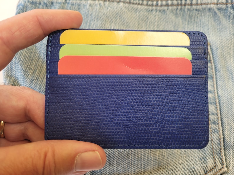 May include: A blue leather card holder with three cards inside. The cards are yellow, green, and red.