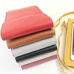 May include: A stack of six different colored leather phone cases. The cases are all closed and are stacked on top of each other. The top case is red, the second case is brown, the third case is gray, the fourth case is black, the fifth case is pink, and the bottom case is a light pink.