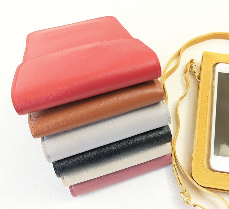 May include: A stack of six different colored leather phone cases. The cases are all closed and are stacked on top of each other. The top case is red, the second case is brown, the third case is gray, the fourth case is black, the fifth case is pink, and the bottom case is a light pink.