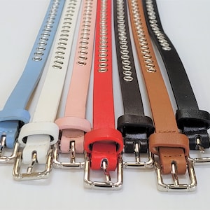 May include: Seven different coloured belts with silver metal accents. The belts are light blue, white, pink, red, black, brown, and dark brown.