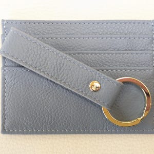 May include: A gray leather card holder with a key ring. The card holder has three slots for cards and a strap with a snap closure.