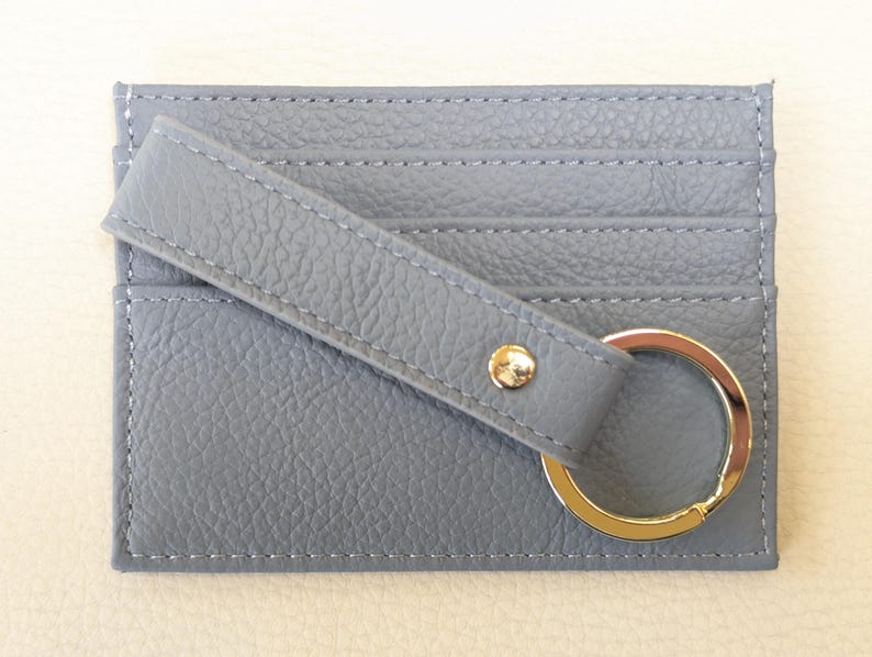 May include: A gray leather card holder with a key ring. The card holder has three slots for cards and a strap with a snap closure.