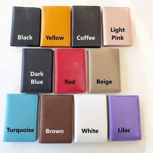 May include: A collection of leather wallets in various colors, including black, yellow, coffee, light pink, dark blue, red, beige, turquoise, brown, white, and lilac. Each wallet is labeled with its respective color.