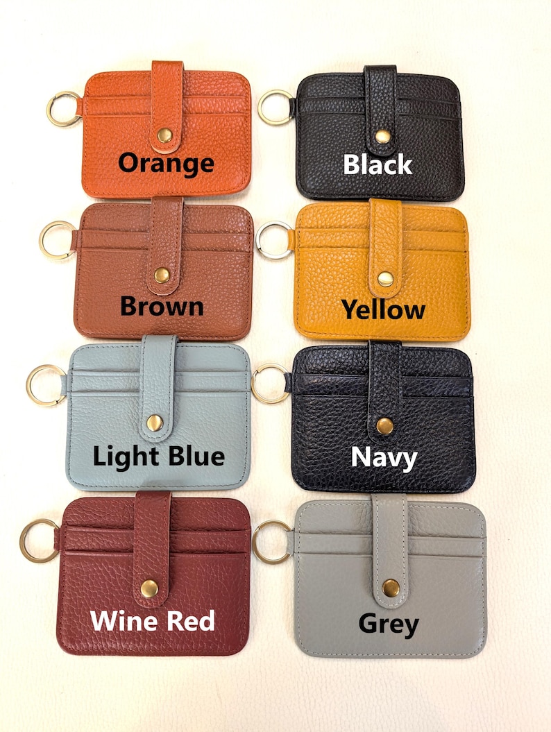 May include: A collection of leather cardholders in various colors, including orange, black, brown, yellow, light blue, navy, wine red, and grey. Each cardholder has a key ring and a snap closure. The text "Orange", "Black", "Brown", "Yellow", "Light Blue", "Navy", "Wine Red", and "Grey" are displayed.