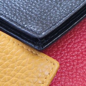 May include: Close-up of three leather textures: black, yellow, and red. The black leather appears to be a wallet or similar item, with visible stitching. The yellow leather is a lighter shade, and the red leather is a deeper tone.
