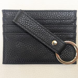 May include: Black leather card holder with a gold metal ring and a strap. The card holder has multiple slots for cards.