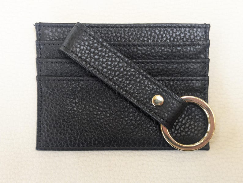 May include: Black leather card holder with a gold metal ring and a strap. The card holder has multiple slots for cards.