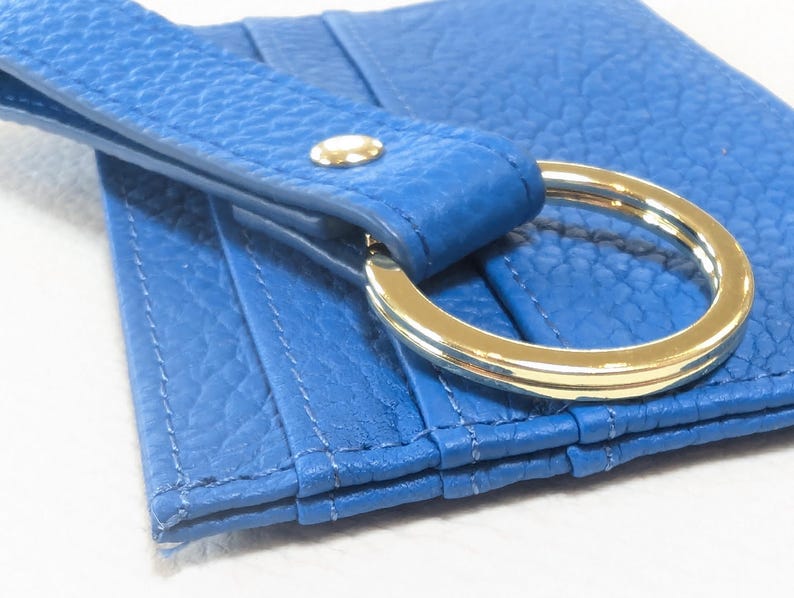 May include: A blue leather card holder with a gold metal ring attached. The card holder has multiple slots for cards and a flap that closes with a snap.